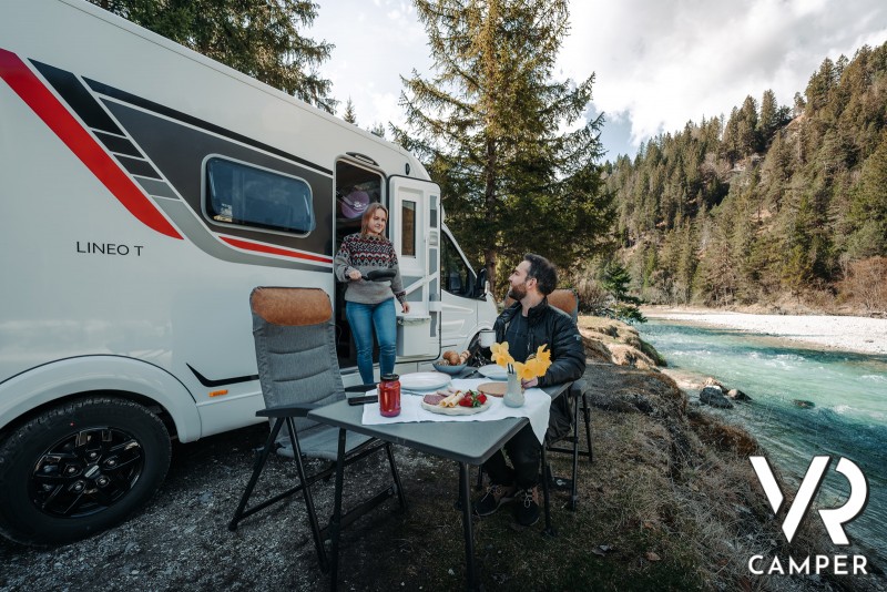 coppia che fa colazione con tavolino davanti a camper Burstner Lineo in riva al fiume