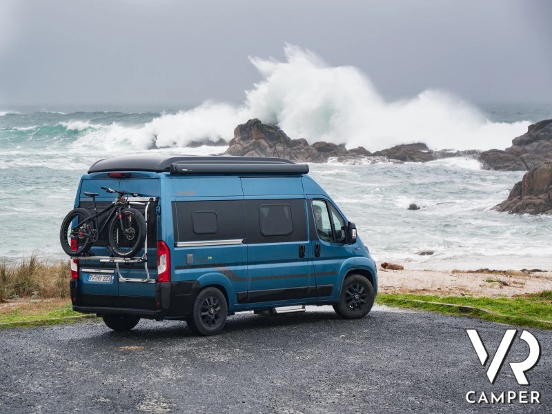 camper furgonato blu in riva al mare mosso con onde alte
