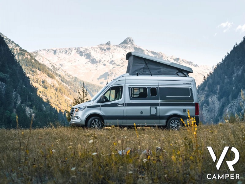 camper furgonato su prato fiorito con montagne sullo sfondo