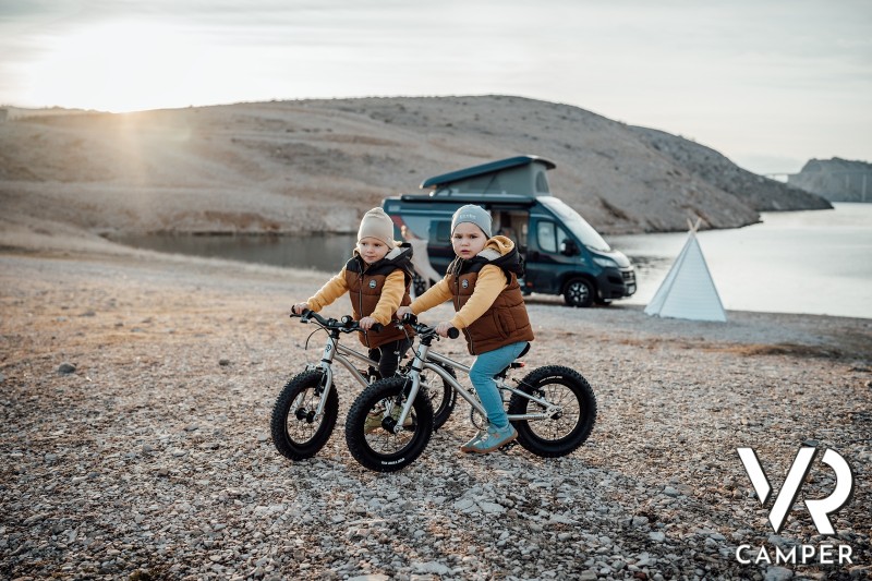 Due bimbi in bicicletta sulla spiaggia, con camper sullo sfondo