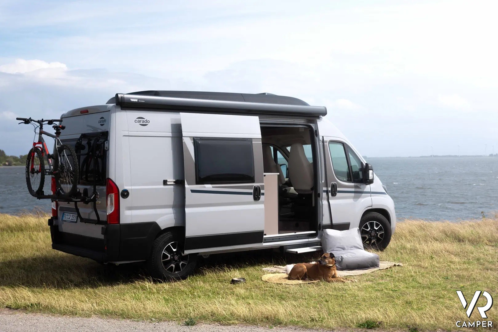 Camper furgonato Carado in riva al mare, con portellone aperto e cane davanti