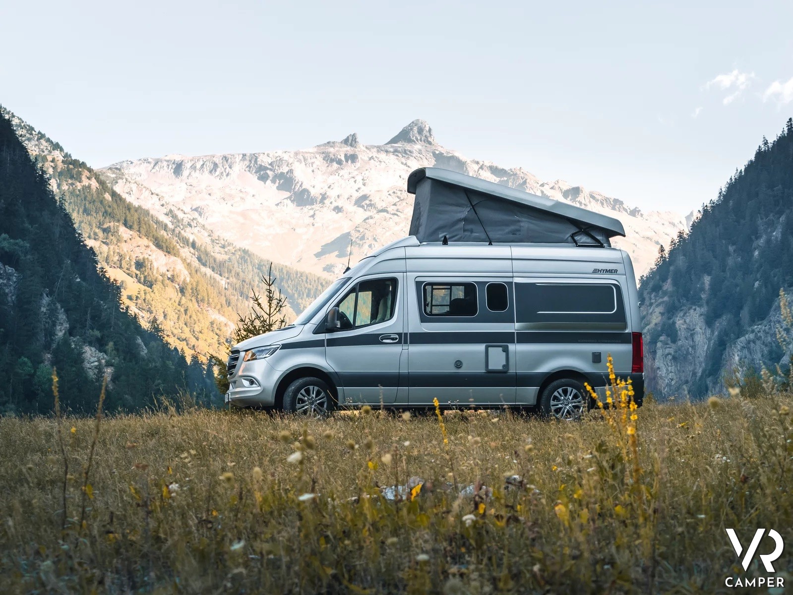camper furgonato su prato di fiori con panorama di montagna