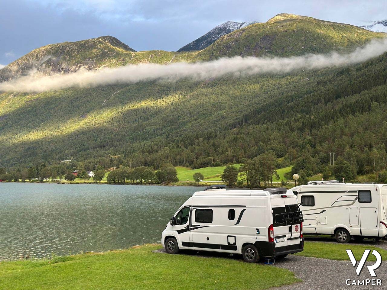 tre camper parcheggiati su prato con lago e montagne
