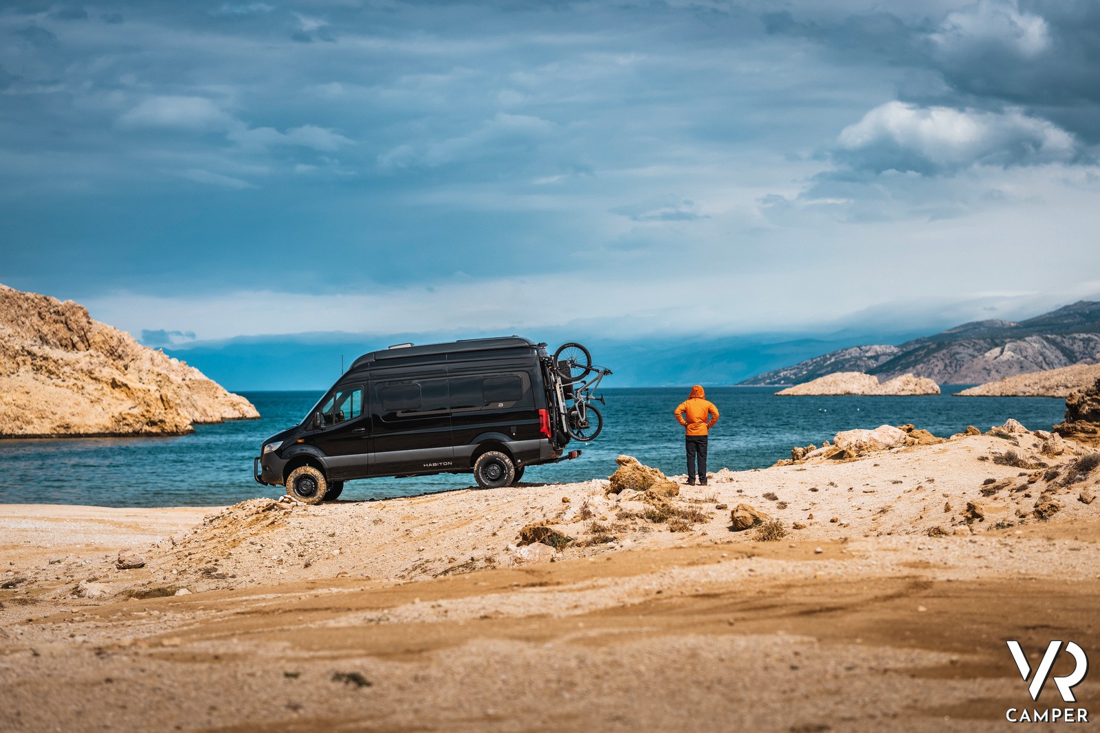 camper van nero sulla costa vicino al mare con uomo felpa arancione